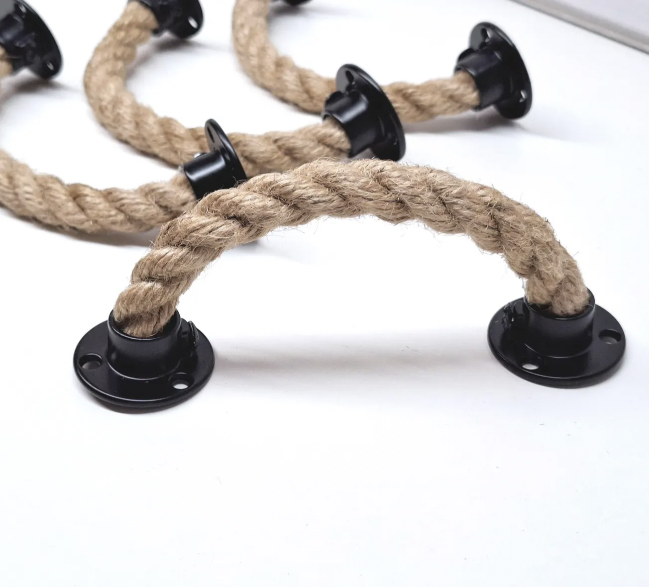 Close-up of rustic rope drawer pulls featuring thick twisted jute rope handles secured with black metal mounting plates, ideal for coastal, nautical, or farmhouse-style furniture and cabinetry updates.